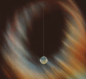 A pendulum with a spherical weight swinging in front of a blurred, multicolored background.